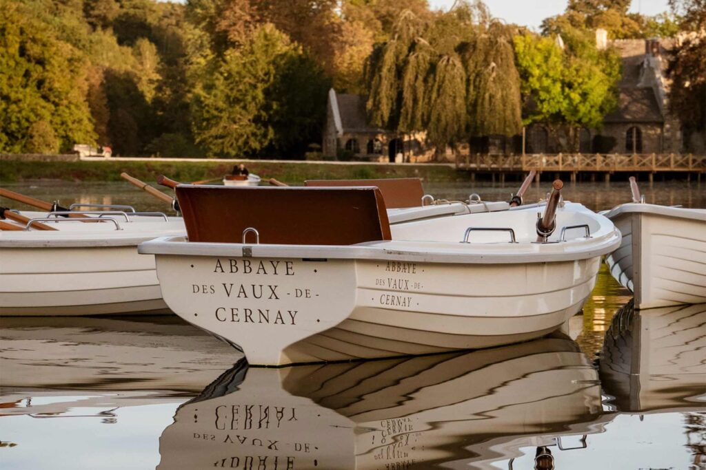 A small row boat in a creek with Abbaye des Vaux-de-Cernay written on its rear. 