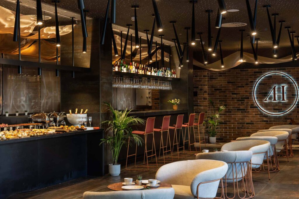 A breakfast buffet in a warmly lit restaurant. Red stalls line the bar.
