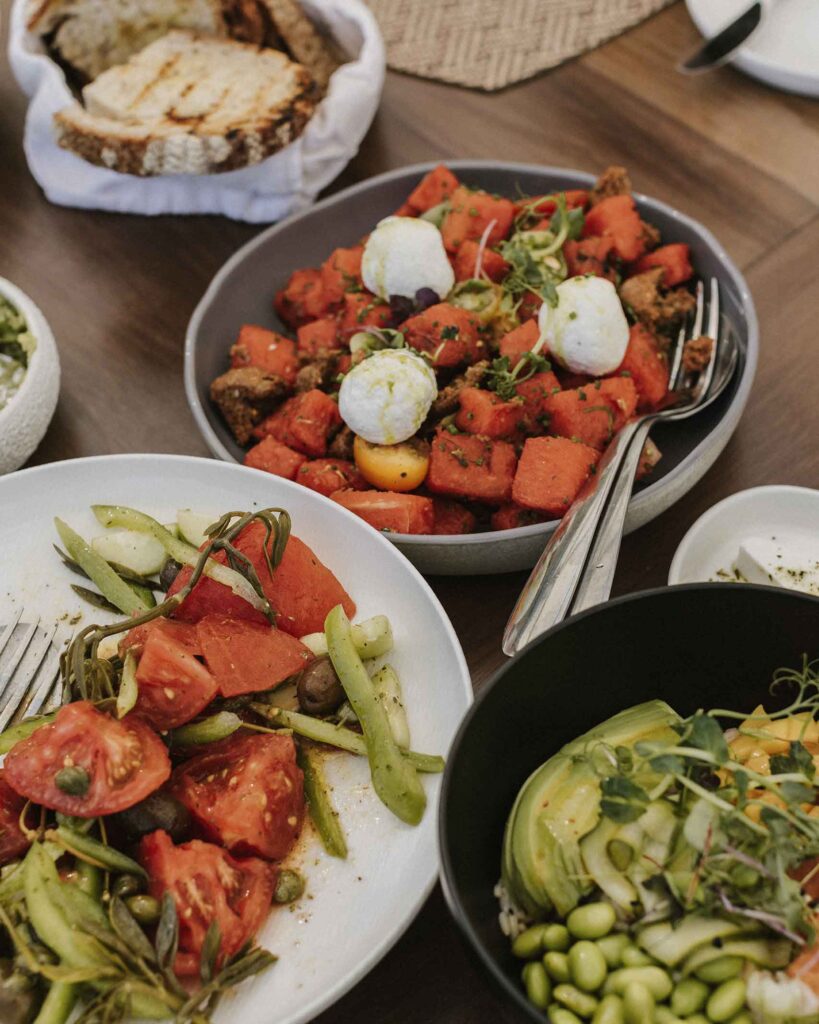 Contempary greek home cooking, three plates of salads with tomatos, beans and other vegetables and bread basket