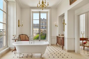 A grand white bathroom with a freestanding tub and tall window - Chic stays outside of Paris.
