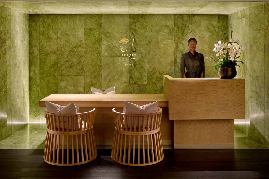 A spa receptionist smiling from behind the reception desk at the Mandarin Oriental Mayfair Spa. A treatment here belongs on any experiential gift guide