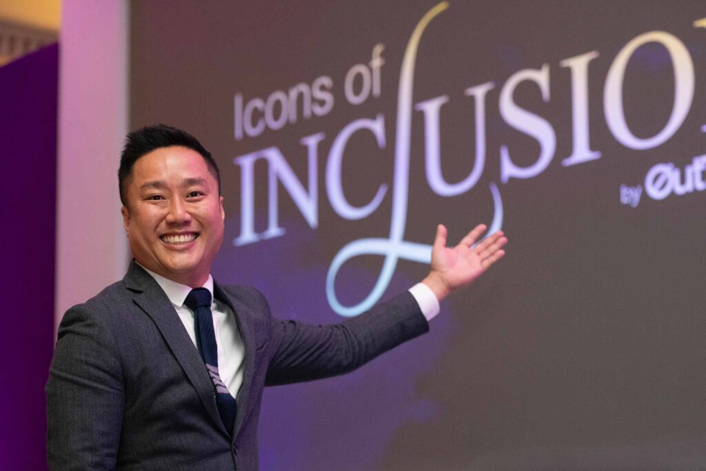 Uwern Jong, Experientialist-in-Chief of OutThere pointing to Icons of Inclusion backdrop at 2024's event