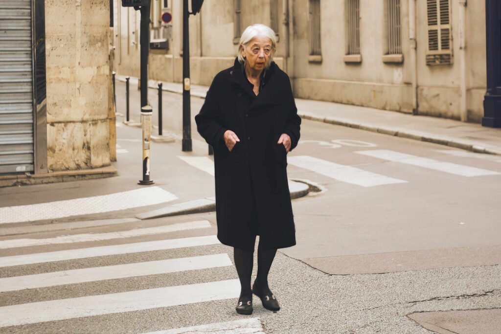 An elderly woman crosses the street, one of many postcards from Paris, France