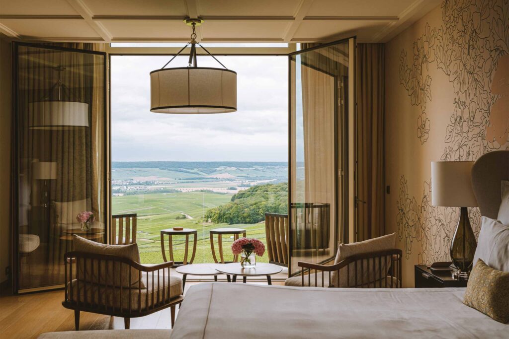 A stylish suite bedroom with open balcony doors revealing the French countryside at the Royal Champagne Hotel & Spa.