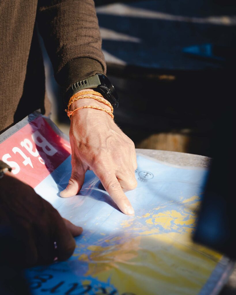 Person in a dark green jacket (we can only see their arm), black wristwatch and orange friendship bracelets points to a map of the Stockholm Archipelago