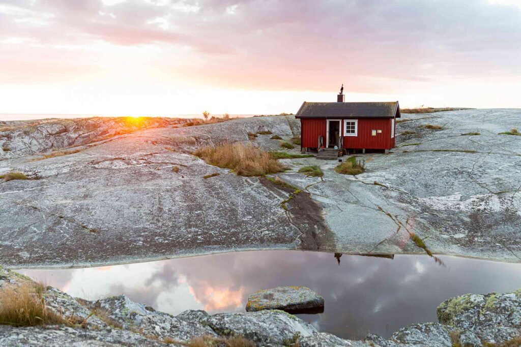 A red traditional Swedish island shed and house sits on top of a rocky island