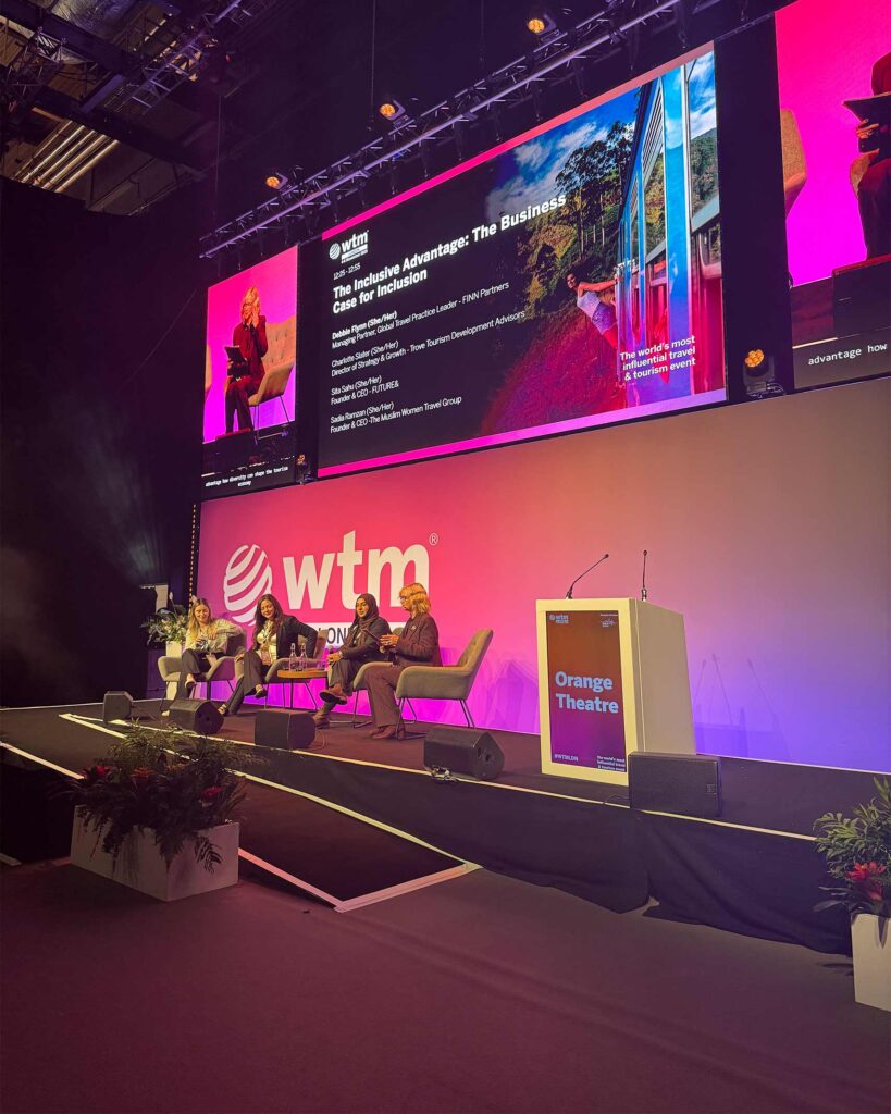 A diverse panel of four women sits on stage for a discussion titled “The Inclusive Advantage: The Business Case for Inclusion,” projected on a large screen.